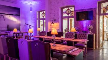 A dining area with a long wooden table, multiple chairs, and ambient purple lighting.