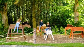 Children can play on the horse-shaped benches in a forested area.