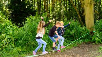 Three children playing on a rope bridge in a forested area.