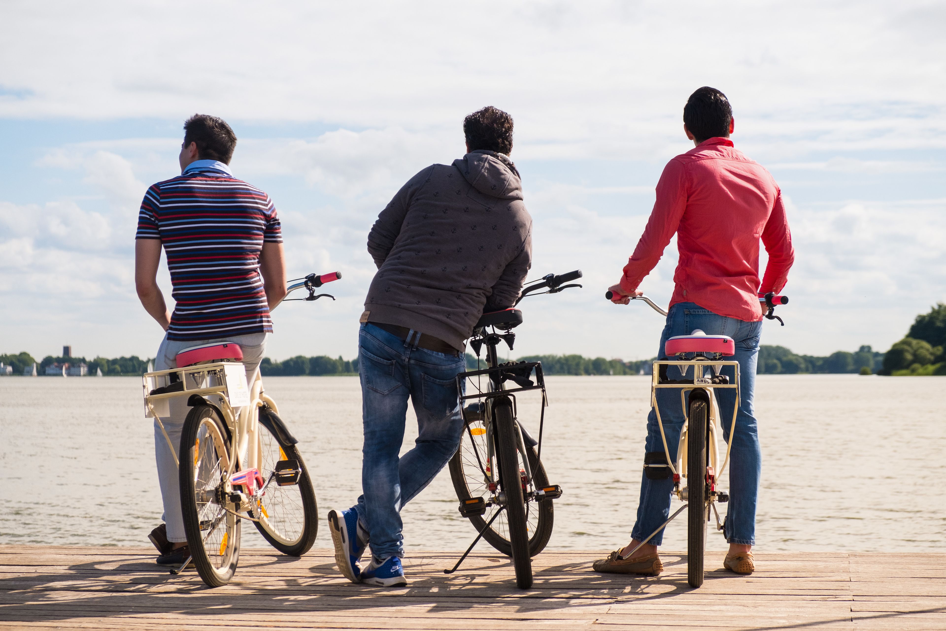 Three men on bicycles on a wooden dock by a lake.