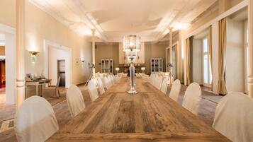 Una larga mesa de conferencias de madera con sillas blancas, una lámpara de araña y suelo alfombrado.