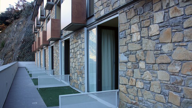 Una hilera de habitaciones de hotel modernas con paredes de piedra y ventanas grandes.