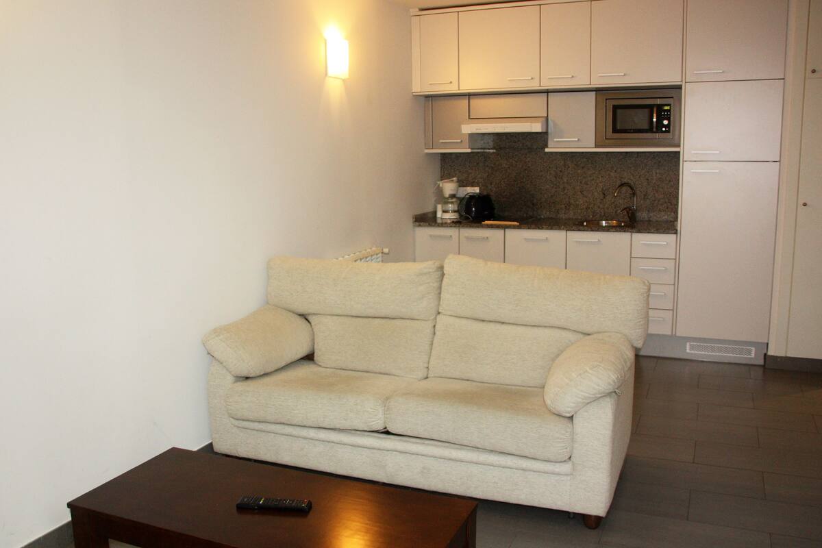 A living room with a beige sofa, a coffee table, and a kitchen area with cabinets and a microwave.