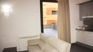 Una sala de estar moderna con sofá, un radiador, una mesita y una zona de cocina con armarios y electrodomésticos.