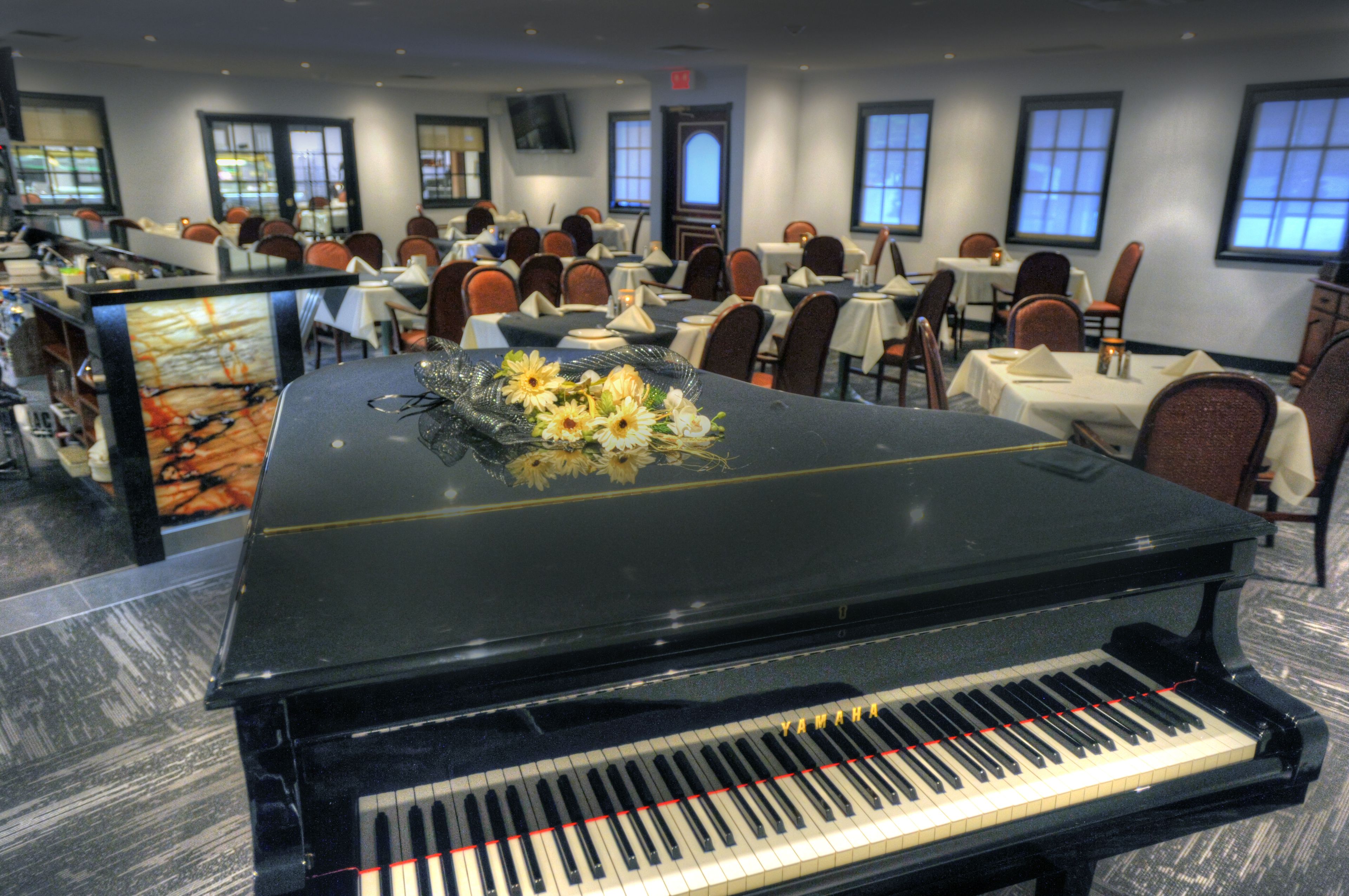 A grand piano in a spacious dining area with multiple tables and chairs.