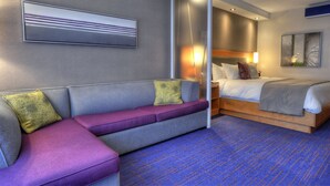 Una habitación de hotel moderna con un sofá gris, una cama y un ventanal grande.