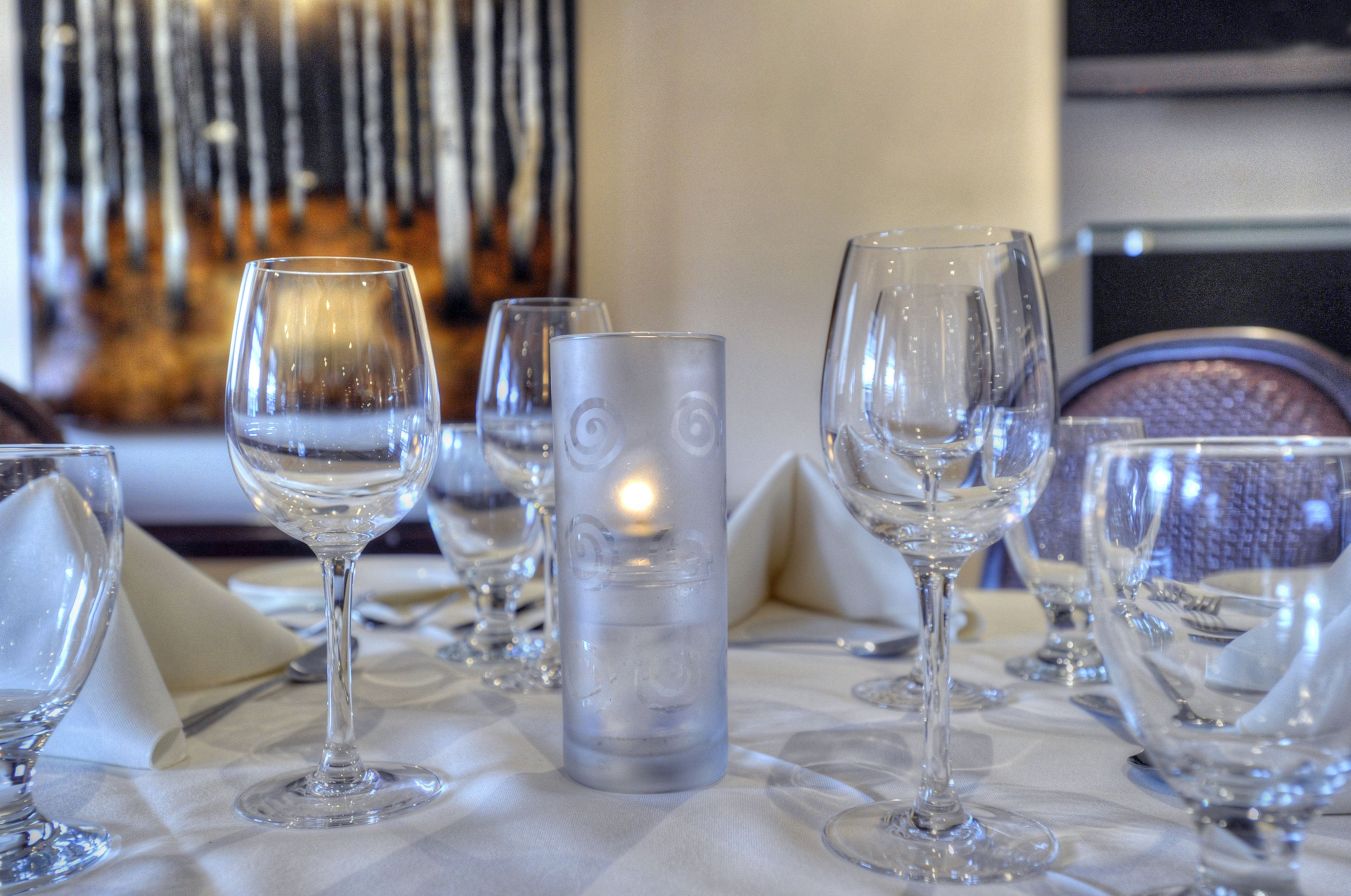 Une table dressée avec de nombreux verres à vin et un porte-bougie en verre transparent.