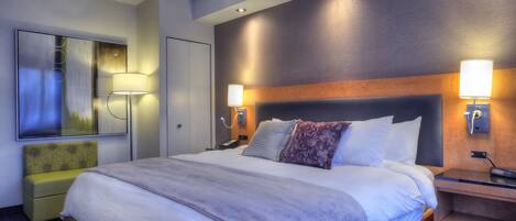 Ein Hotelzimmer mit einem großen Bett, einem Nachttisch, einer Lampe, einem Spiegel und einer kleinen Sitzecke.