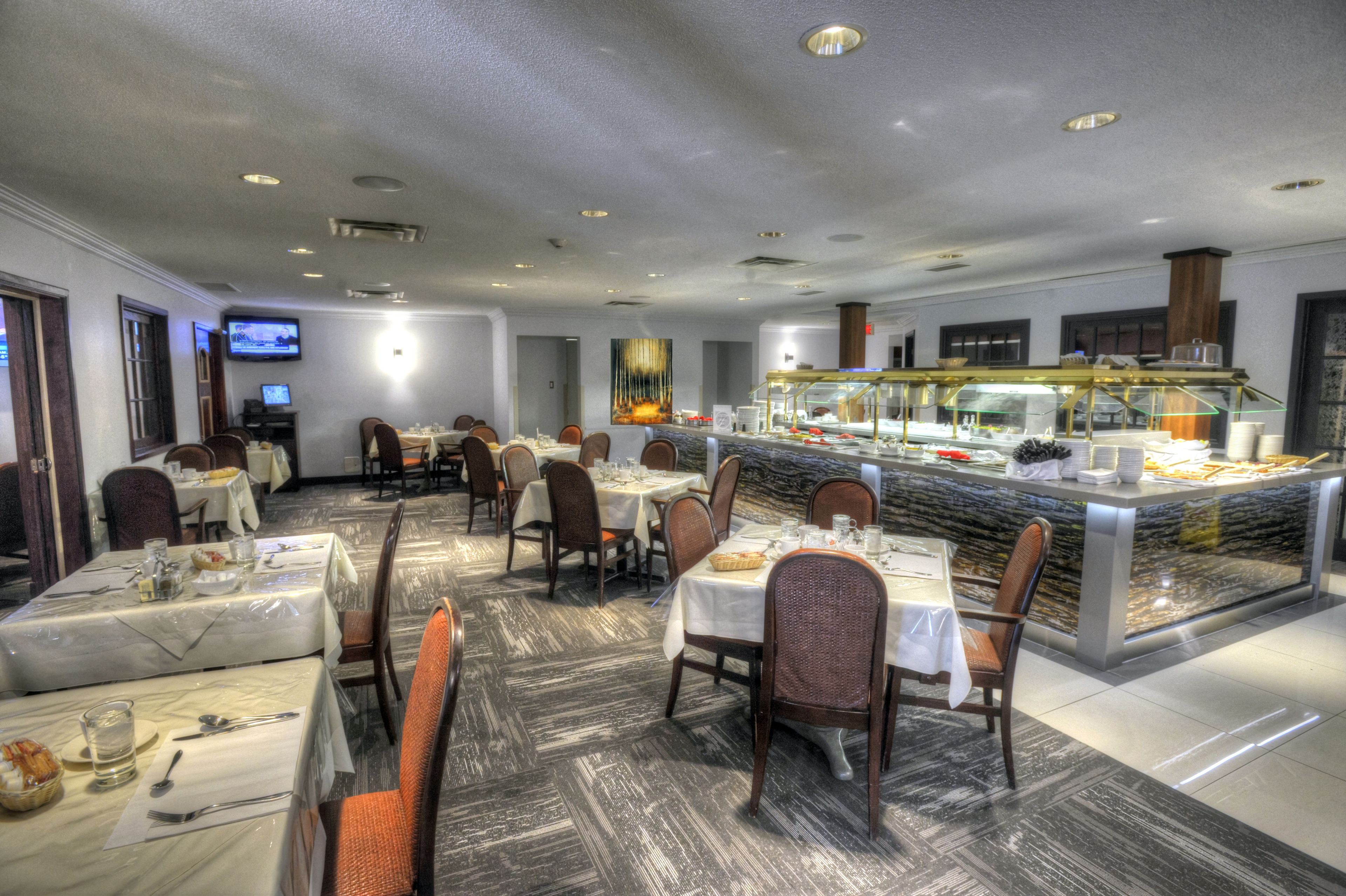 A hotel dining area with multiple tables, chairs, a buffet counter, and a television screen.