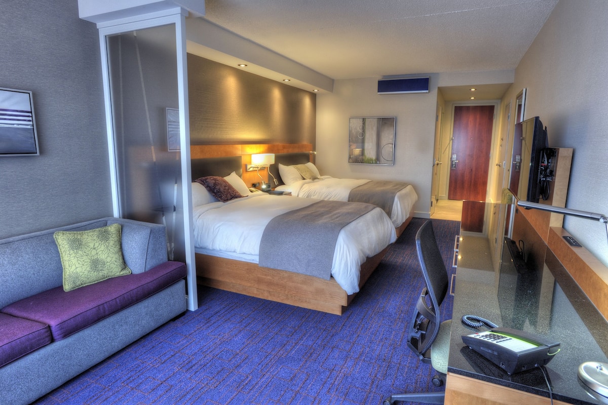A hotel room with a large bed, a sofa, a desk with a telephone, and a mirror.