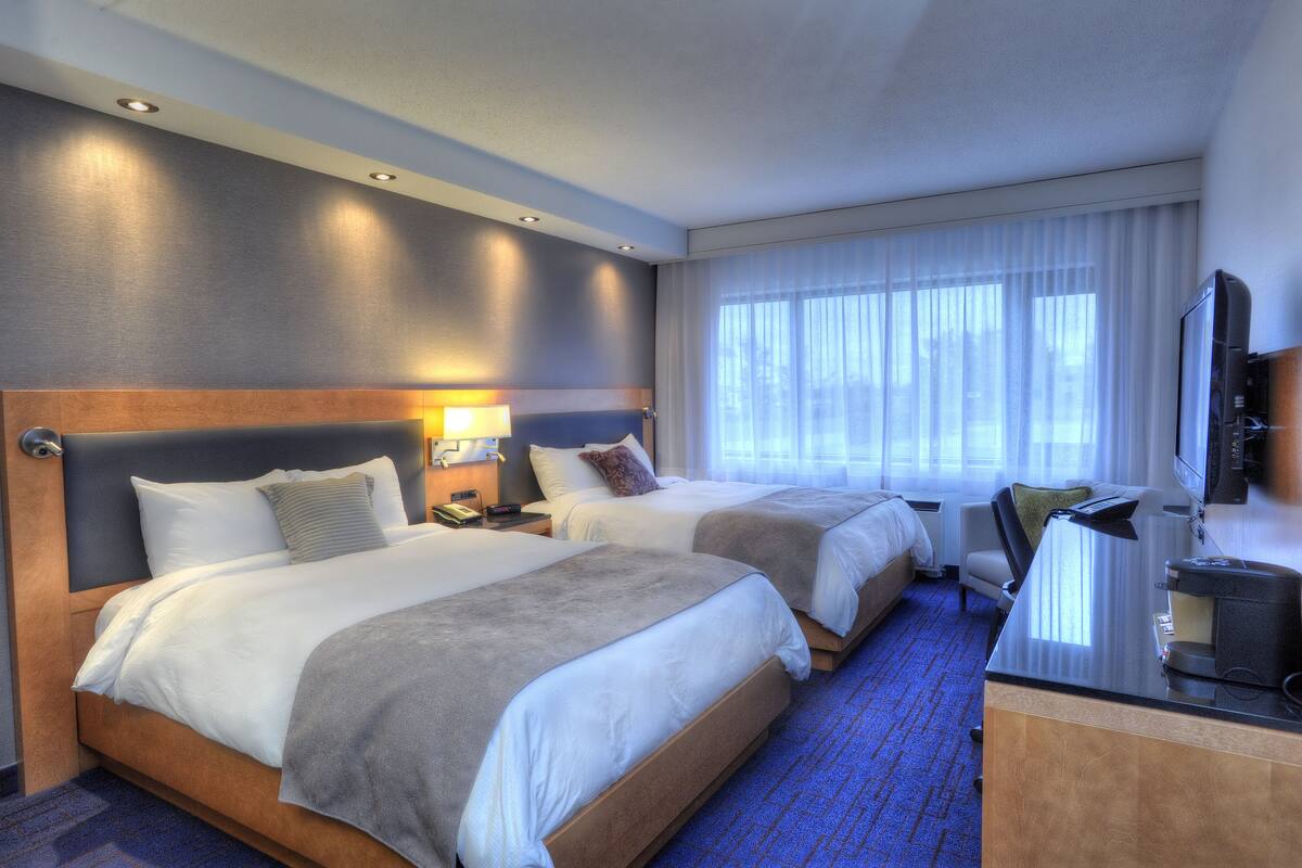 A hotel room with two beds, a desk with a coffee maker, a TV, and a window with curtains.