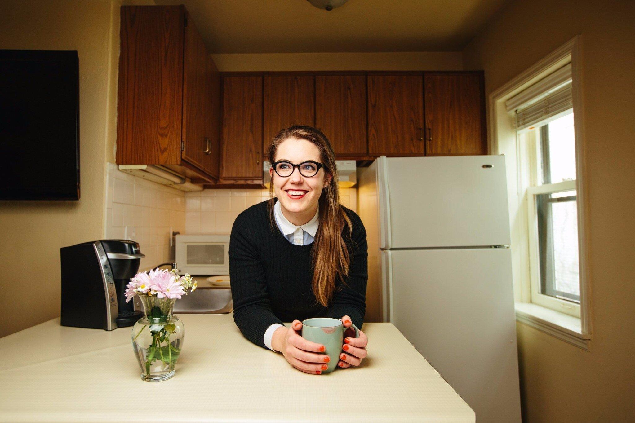 A kitchen with wooden cabinets, a refrigerator, a coffee maker, and a vase with flowers on the counter.