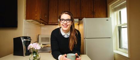 A kitchen with wooden cabinets, a refrigerator, a coffee maker, and a vase with flowers on the counter.