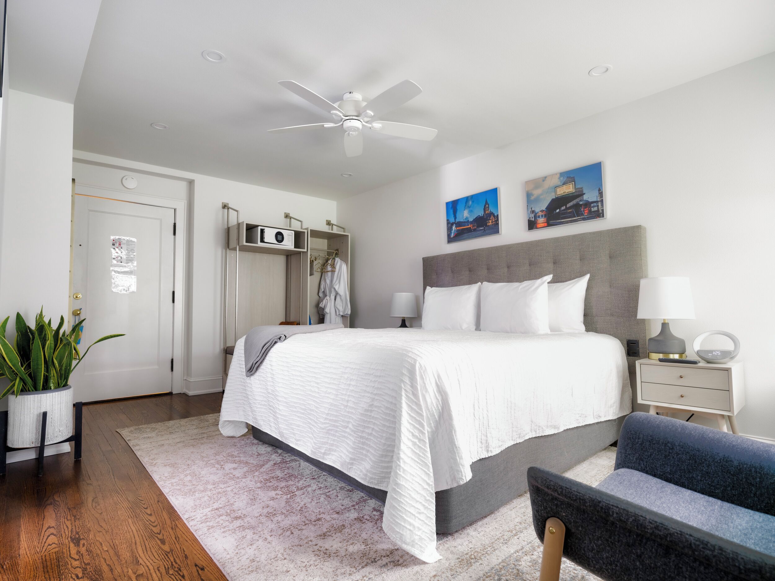Une chambre d’hôtel moderne dotée d’un grand lit, d’un ventilateur de plafond, d’une armoire, d’une table de chevet avec une lampe et de deux œuvres d’art murales.