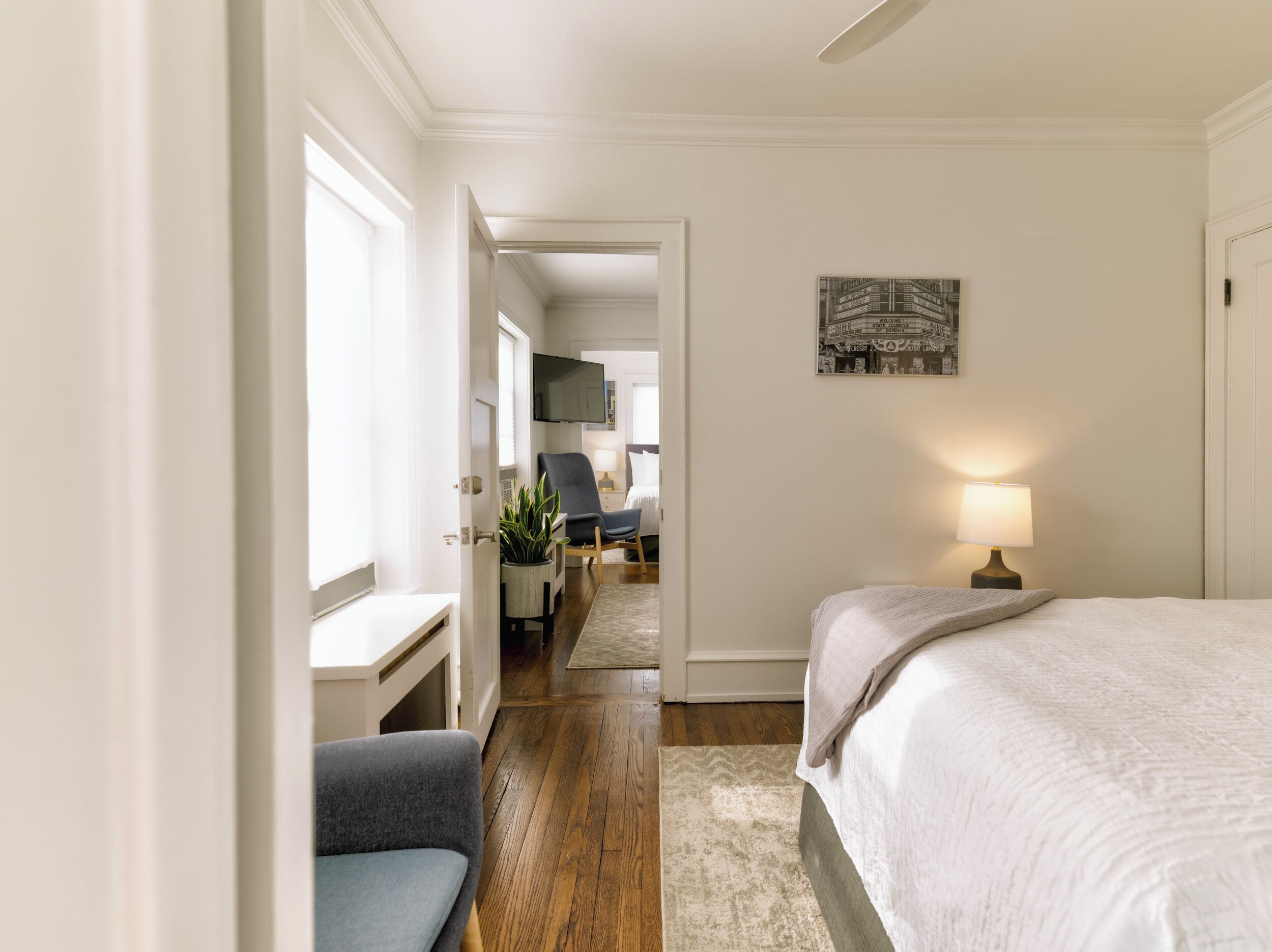 A bedroom with a bed, a desk, a chair, a TV, and a lamp.