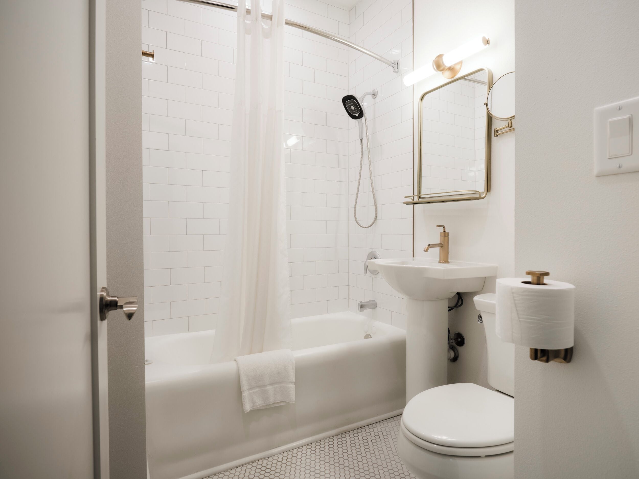 A modern bathroom with a white bathtub, a shower, a sink with a gold faucet, and a toilet.
