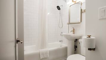 A modern bathroom with a white bathtub, a shower, a sink with a gold faucet, and a toilet.