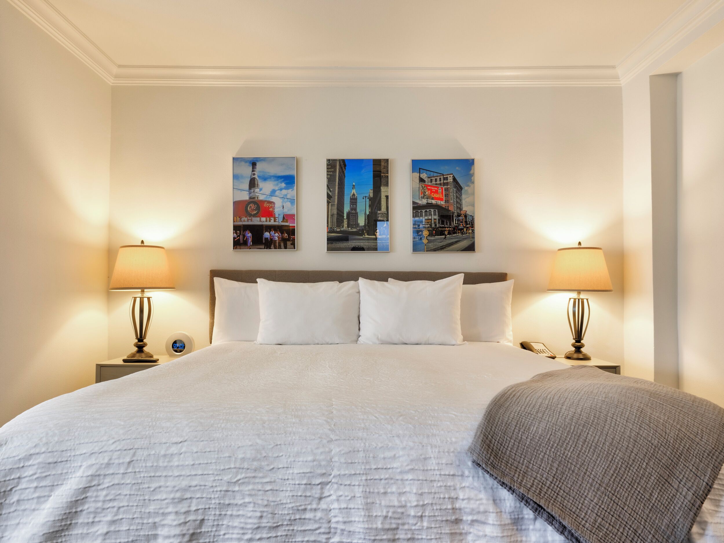 A hotel room with a large bed, two bedside lamps, and three framed pictures on the wall.