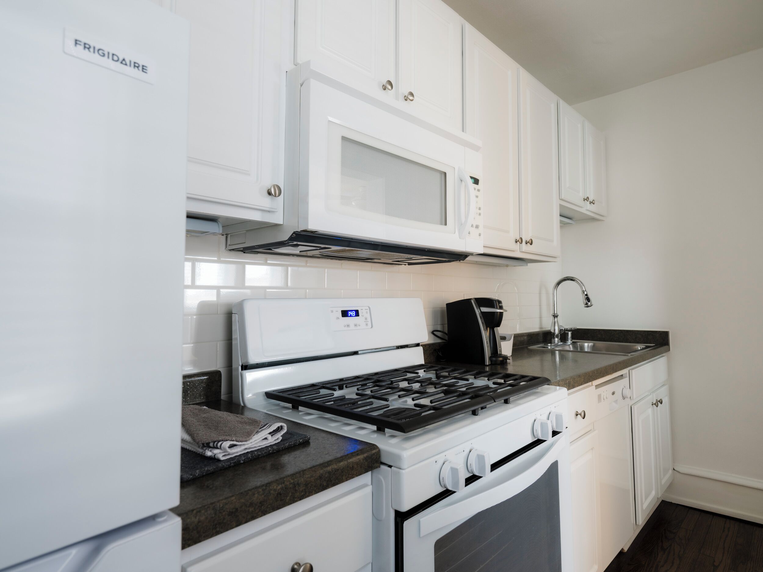 A kitchen with white cabinetry, a stove, a microwave, and a coffee maker.