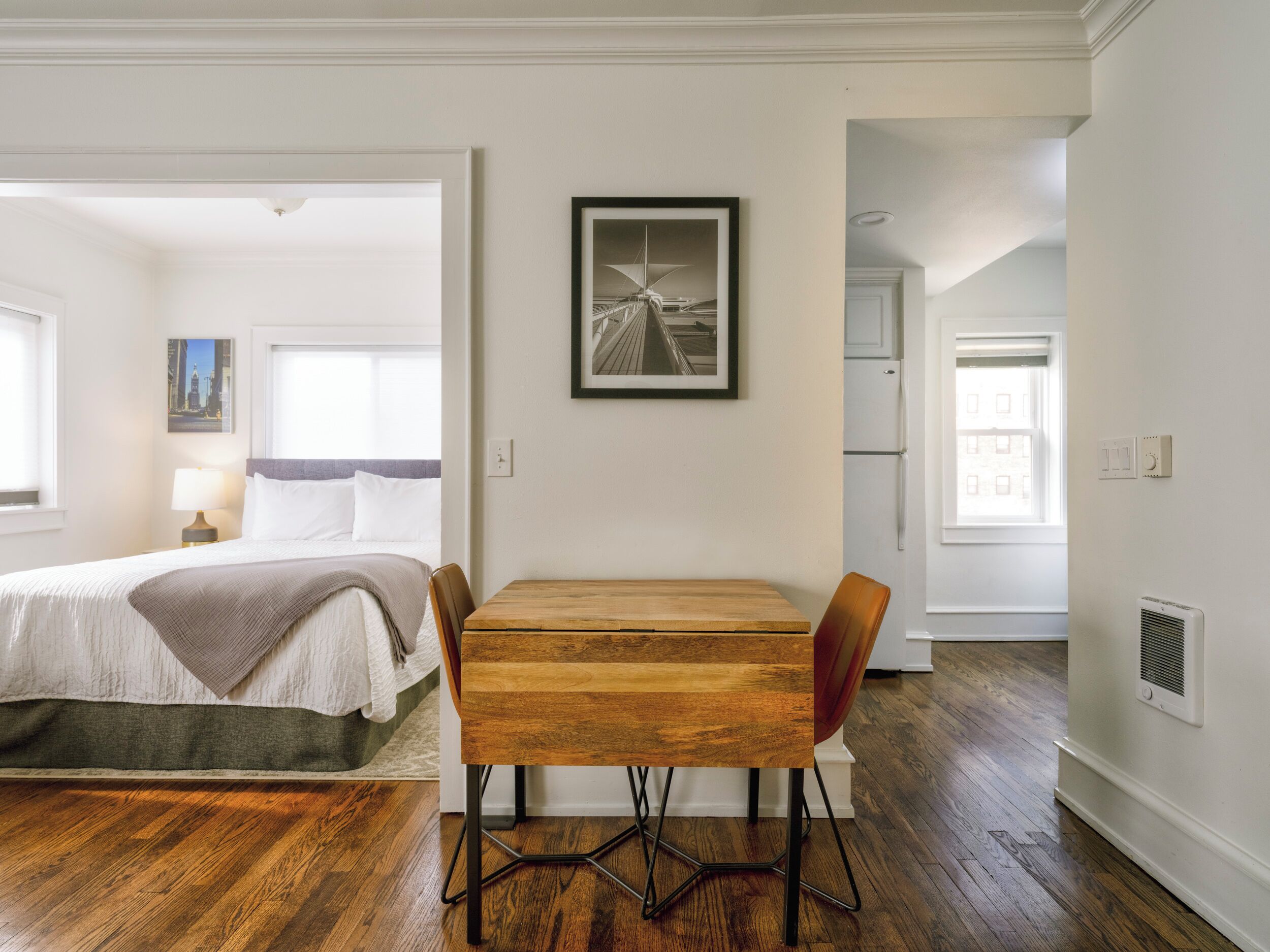 A hotel room with a bed, a wooden table with chairs, a framed picture on the wall, and a view of the city through the window.