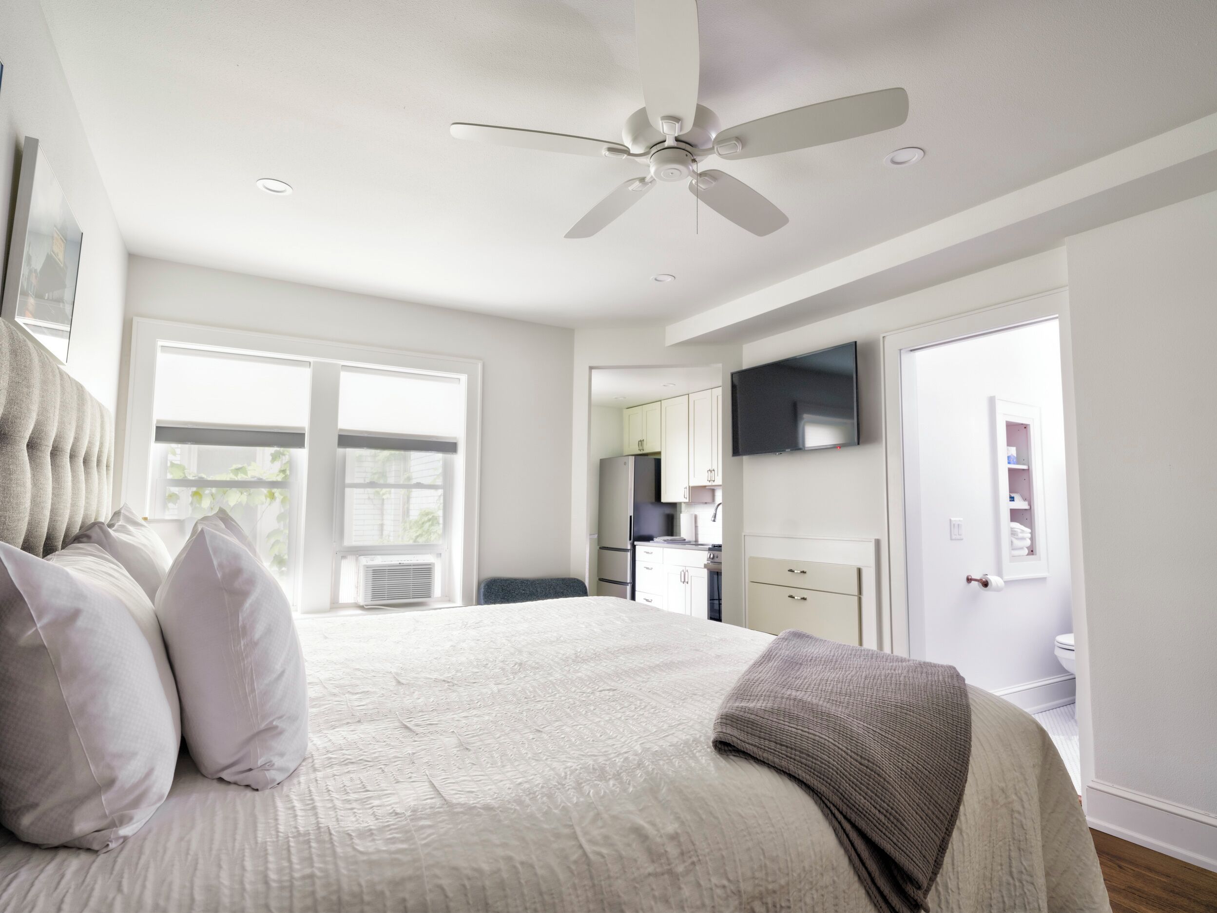 Une chambre avec un lit, un ventilateur de plafond, une fenêtre et une vue sur la cuisine.