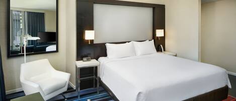 Quarto de hotel com uma cama grande, uma escrivaninha, uma cadeira, uma televisão e um espelho.