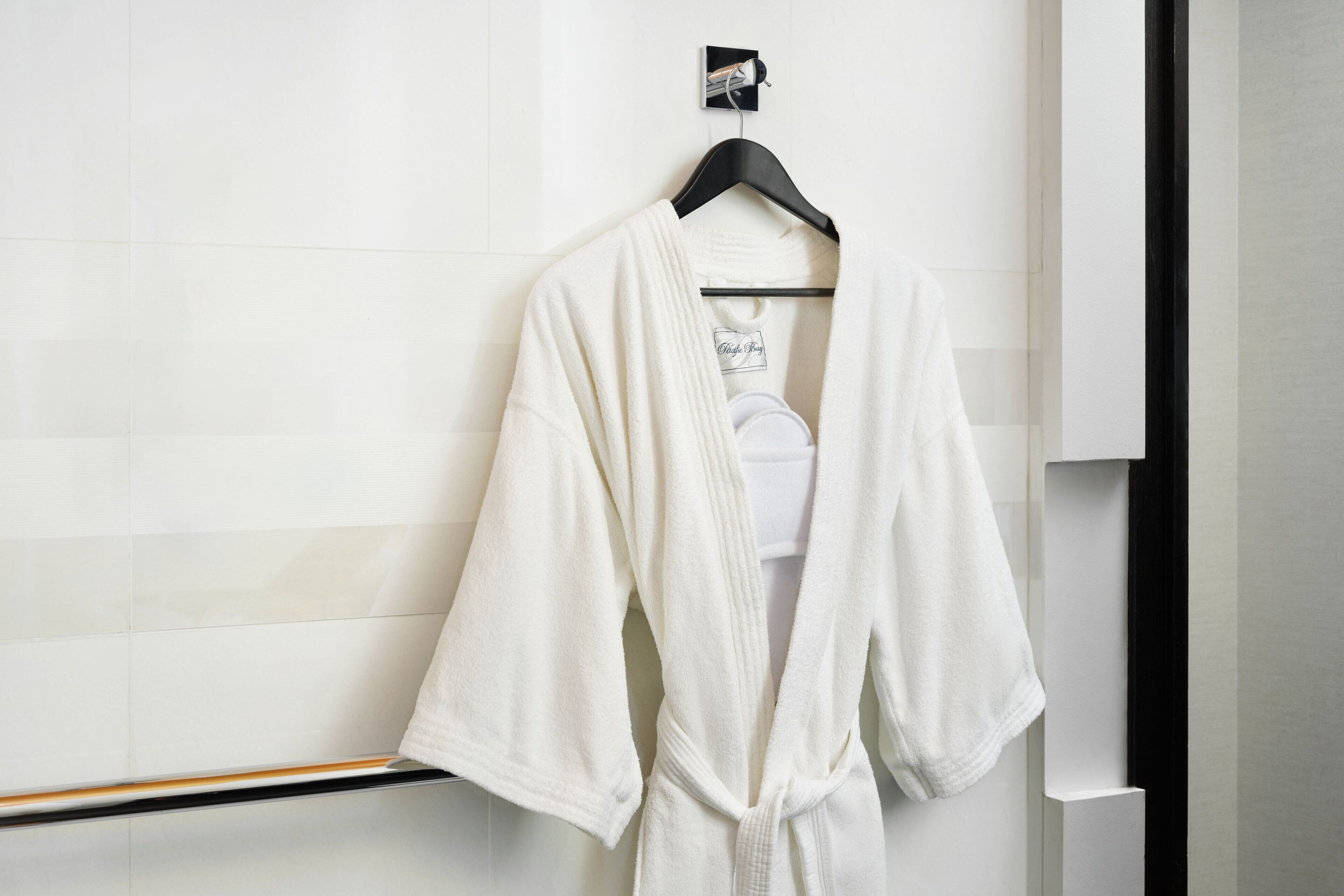 Une robe blanche est suspendue à un cintre noir dans une salle de bain aux carreaux blancs et dont le cadre est noir.