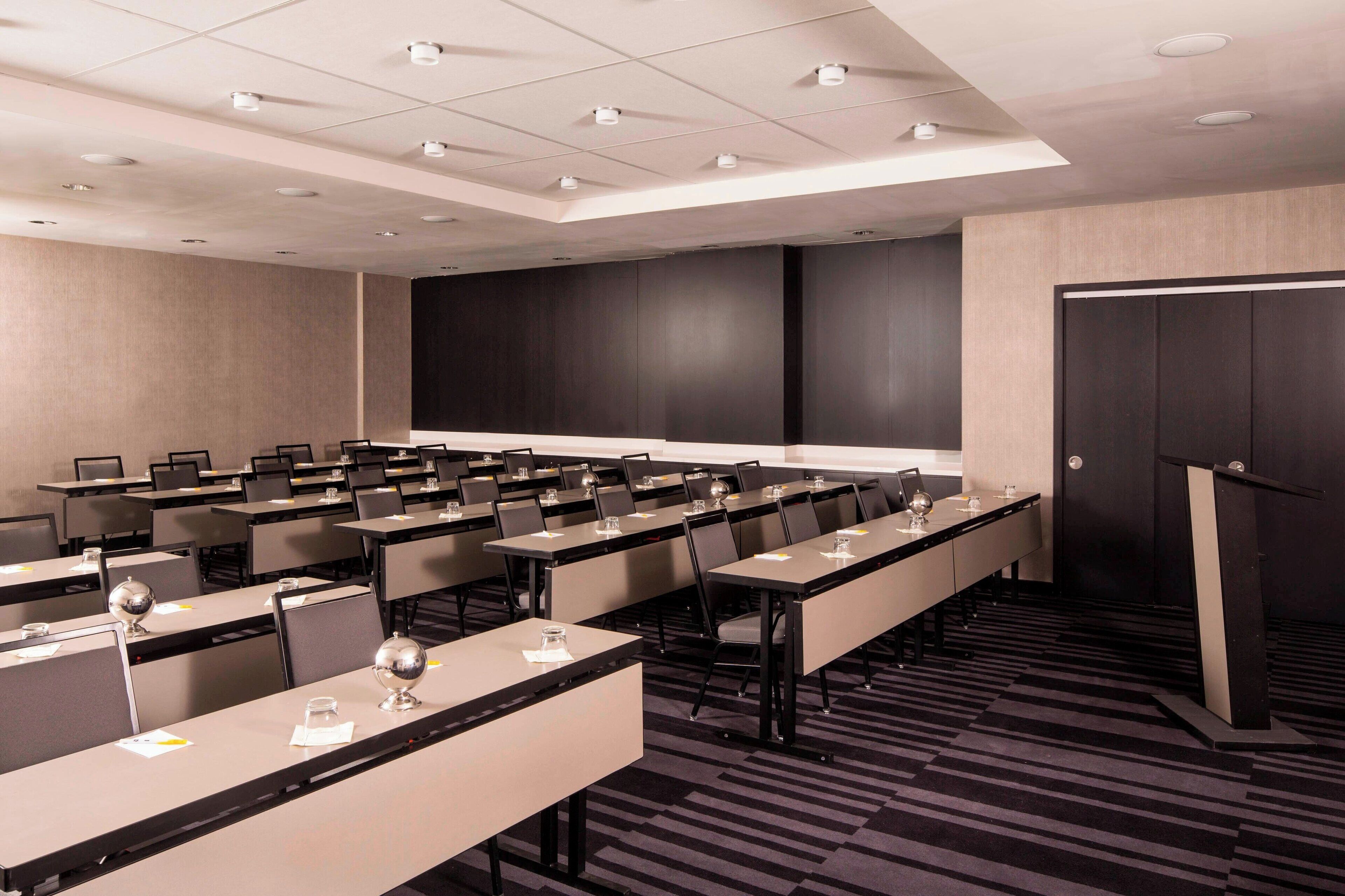 A conference room with rows of tables, chairs, and a podium.