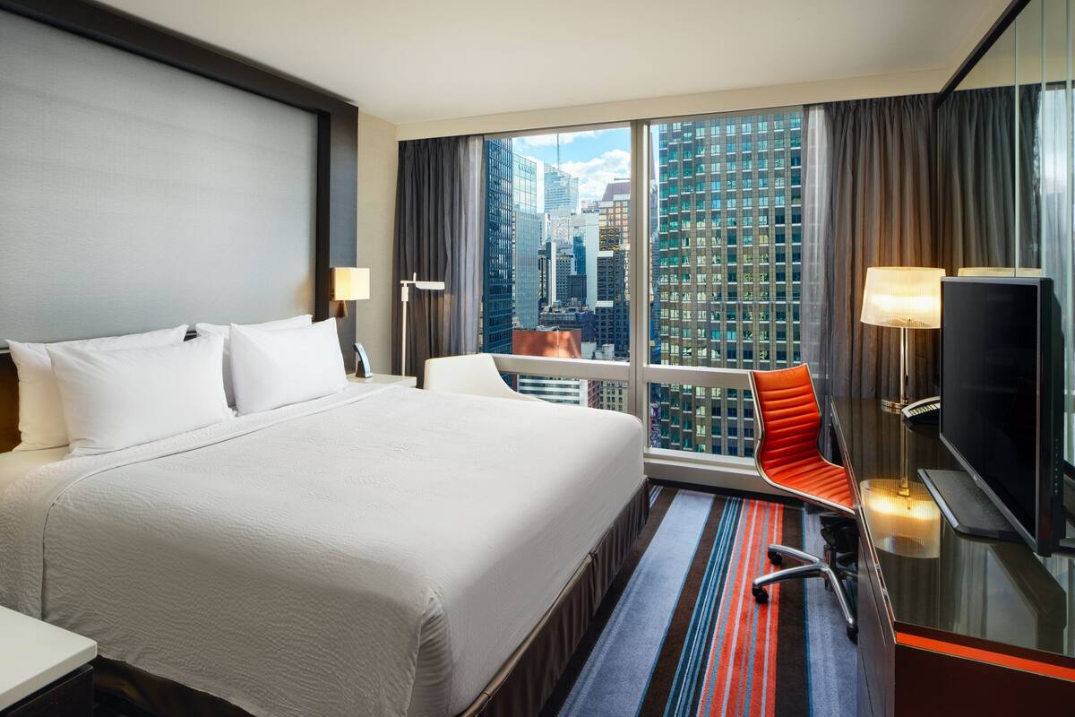 Una habitación de hotel con una cama grande, televisión, escritorio y vistas a la ciudad.