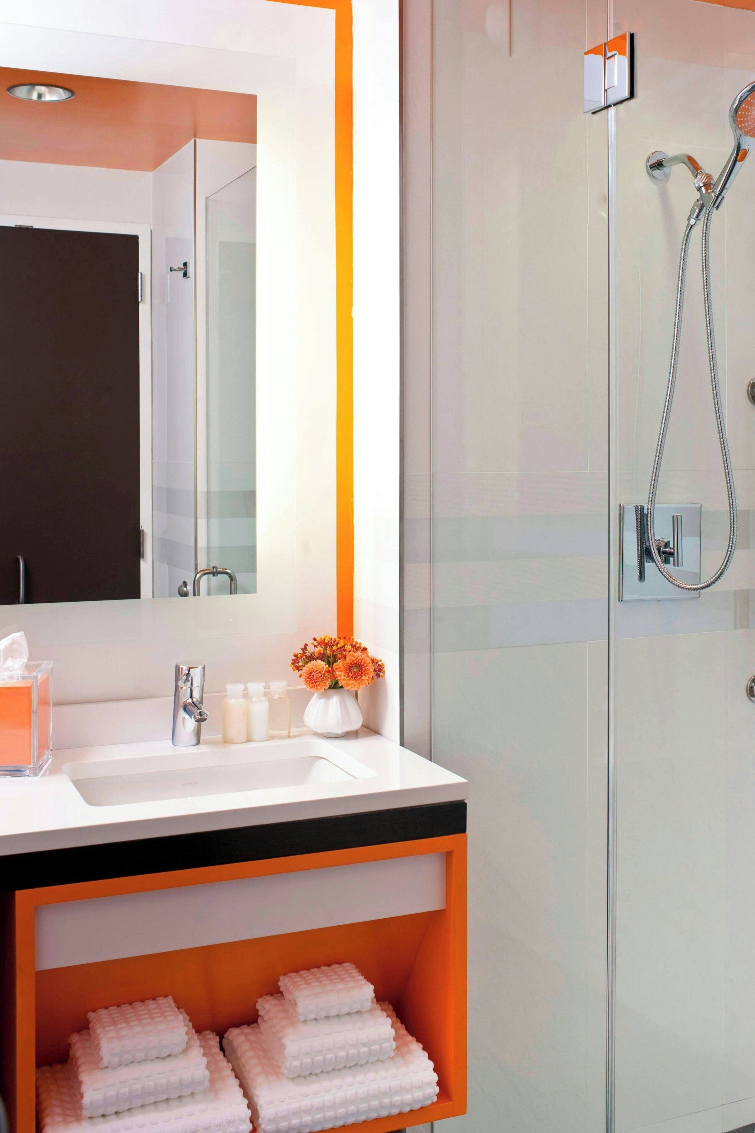 Un baño moderno con cabina de ducha de vidrio, un lavabo blanco con espejo y un estante con toallas dobladas.