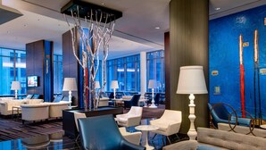 Un moderno vestíbulo de hotel con zonas de estar, una escultura de árbol decorativa y una gran pared azul con arte abstracto.