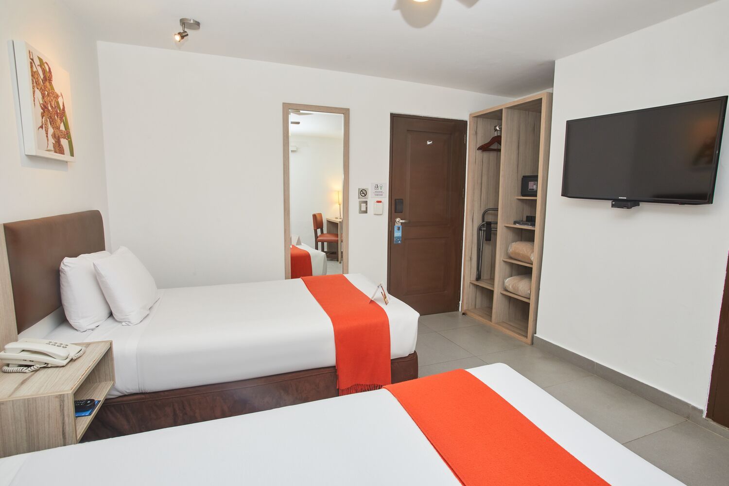 A hotel room with two beds, a TV, a wardrobe, and a desk with a phone.