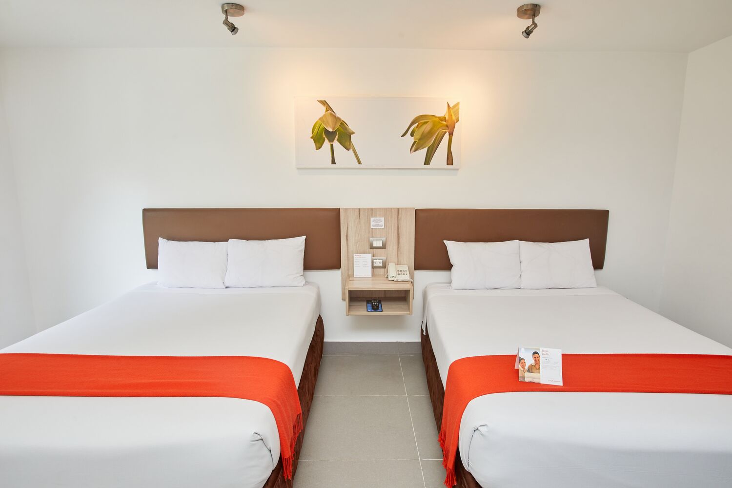 A hotel room with two beds, a nightstand, a wall-mounted phone, and a framed picture of leaves.