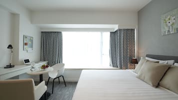 Une chambre d’hôtel avec un lit, un bureau avec un ordinateur portable, une chaise et une fenêtre avec des rideaux à motifs.