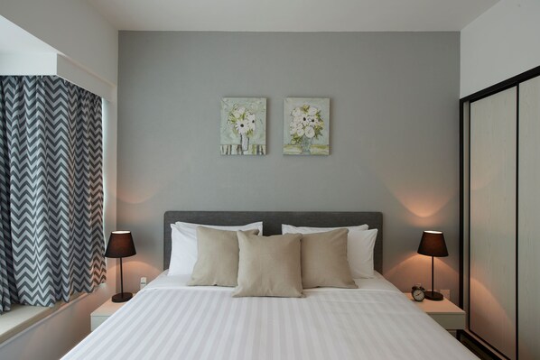 A hotel room with a bed, two bedside tables with lamps, a window with curtains, and two wall-mounted paintings.
