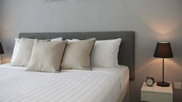 Un lit bien fait, avec du linge de lit blanc et plusieurs oreillers, une table de chevet avec une lampe et un réveil, et deux œuvres d’art accrochées au mur.