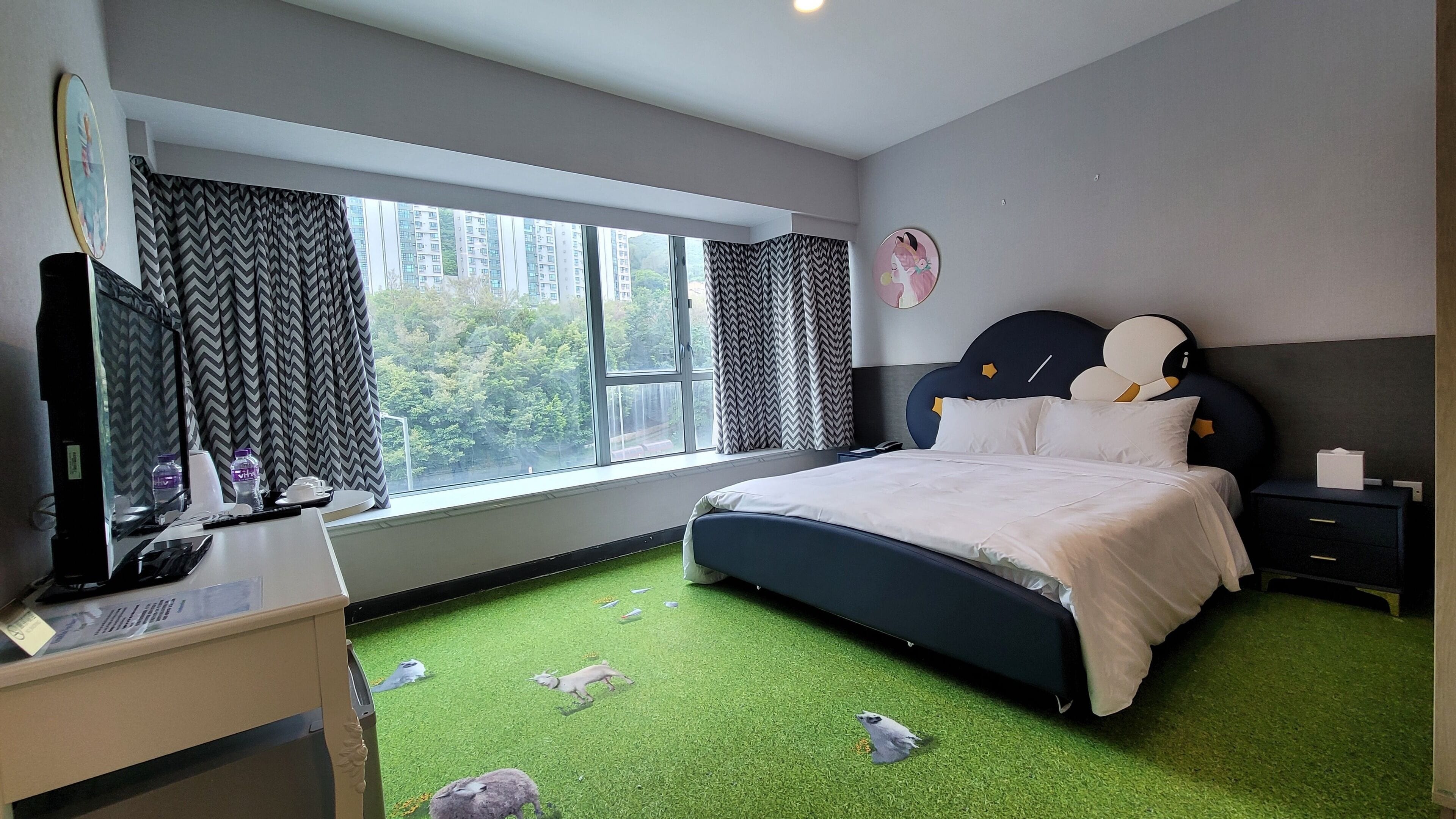 Un dormitorio con cama, escritorio, televisor y ventana con cortinas.