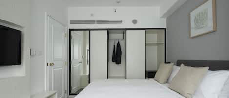 A hotel room with a large bed, a flat-screen TV mounted on the wall, a wardrobe, and a coat rack.