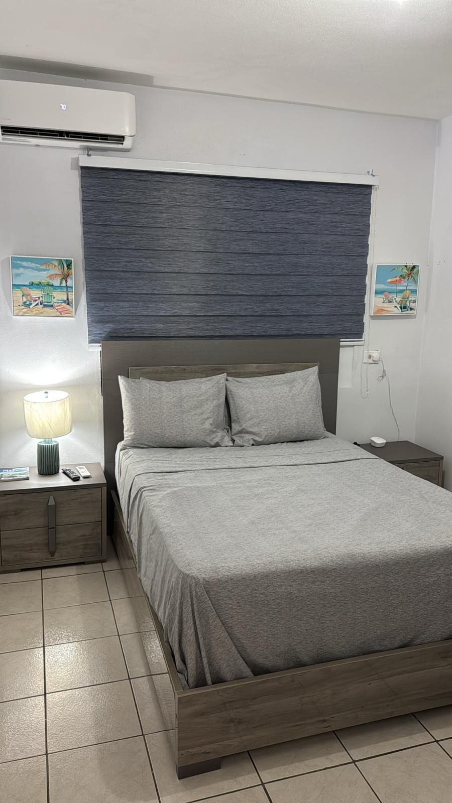 A bedroom with a bed, a nightstand, a lamp, and an air conditioning unit.
