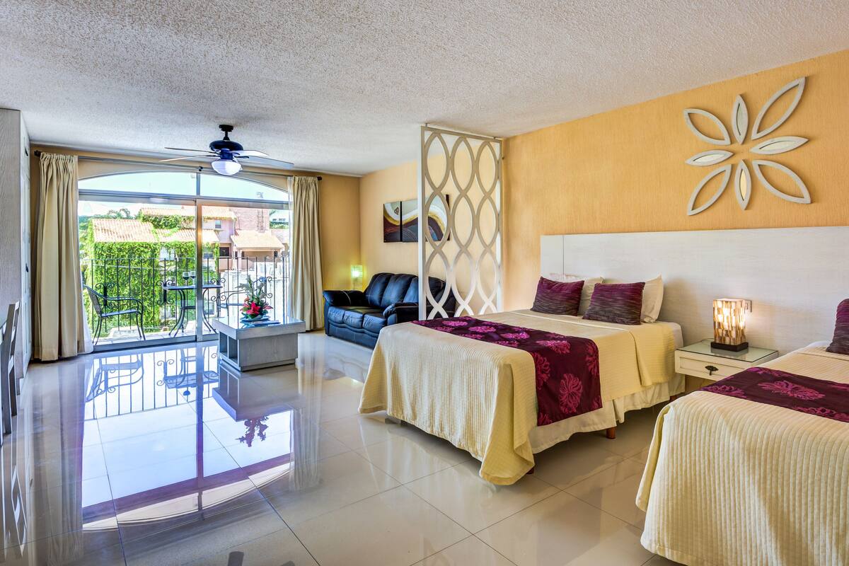 A hotel room with two beds, a balcony, and a view of the cityscape.