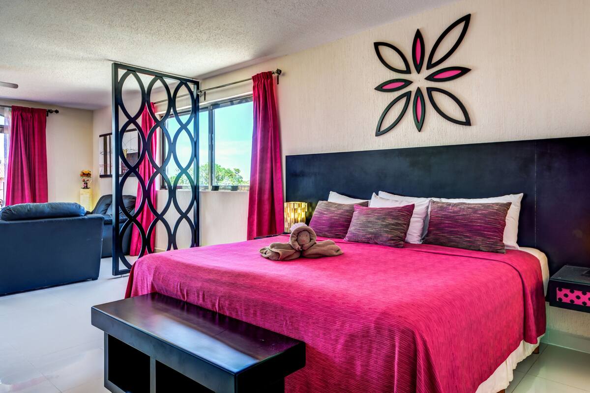A modern bedroom with a large bed, a decorative wall piece, and a view of the outdoors.