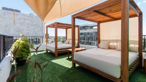 Eine Dachterrasse mit zwei Holzliegen, einem großen Sonnenschirm und einem Topfpflanzen.