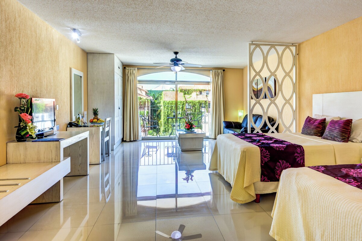 A hotel room with a balcony, a bed, a desk, and a chair.