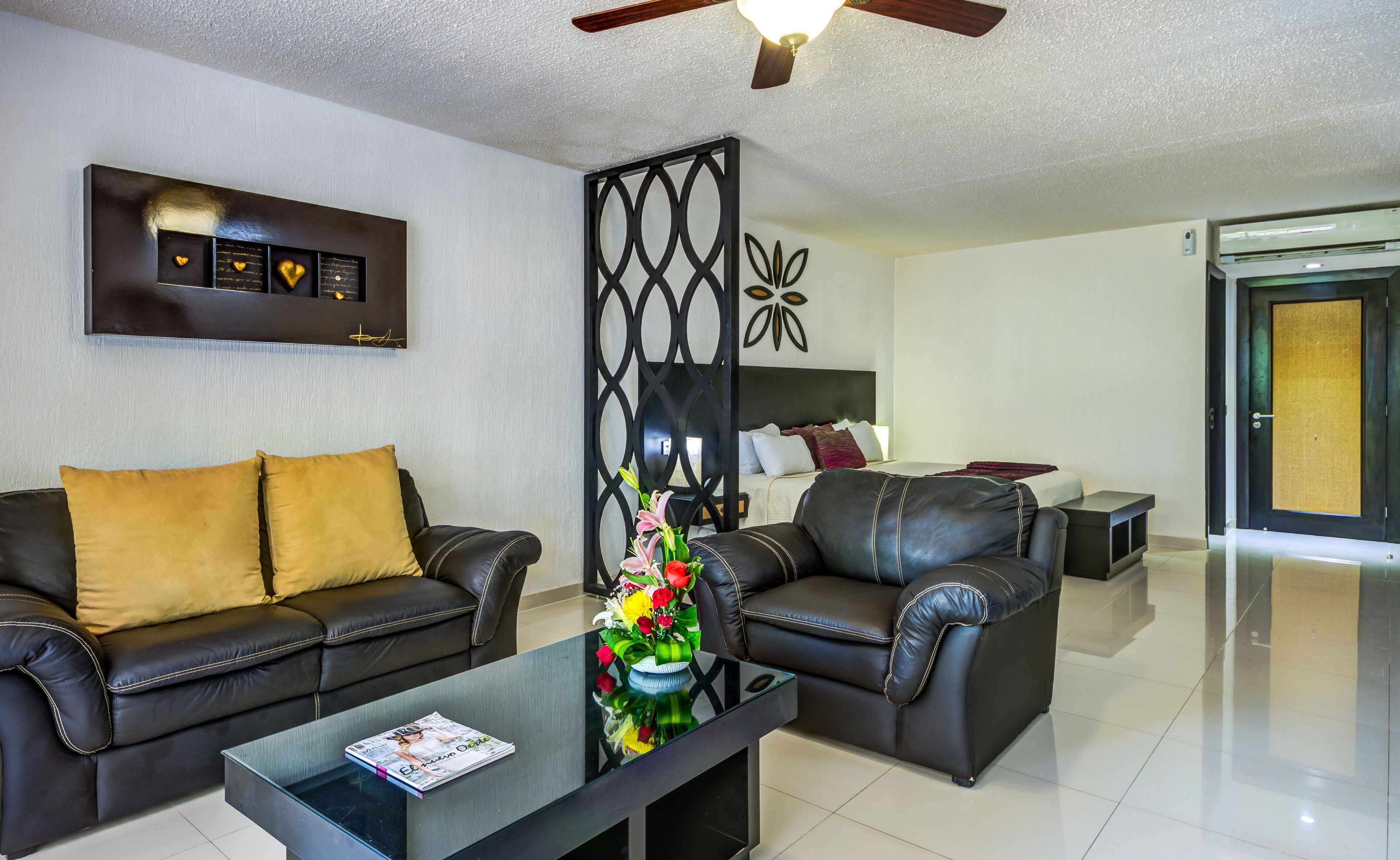 A modern living room with a black leather sofa, a glass coffee table, and a decorative wall piece.