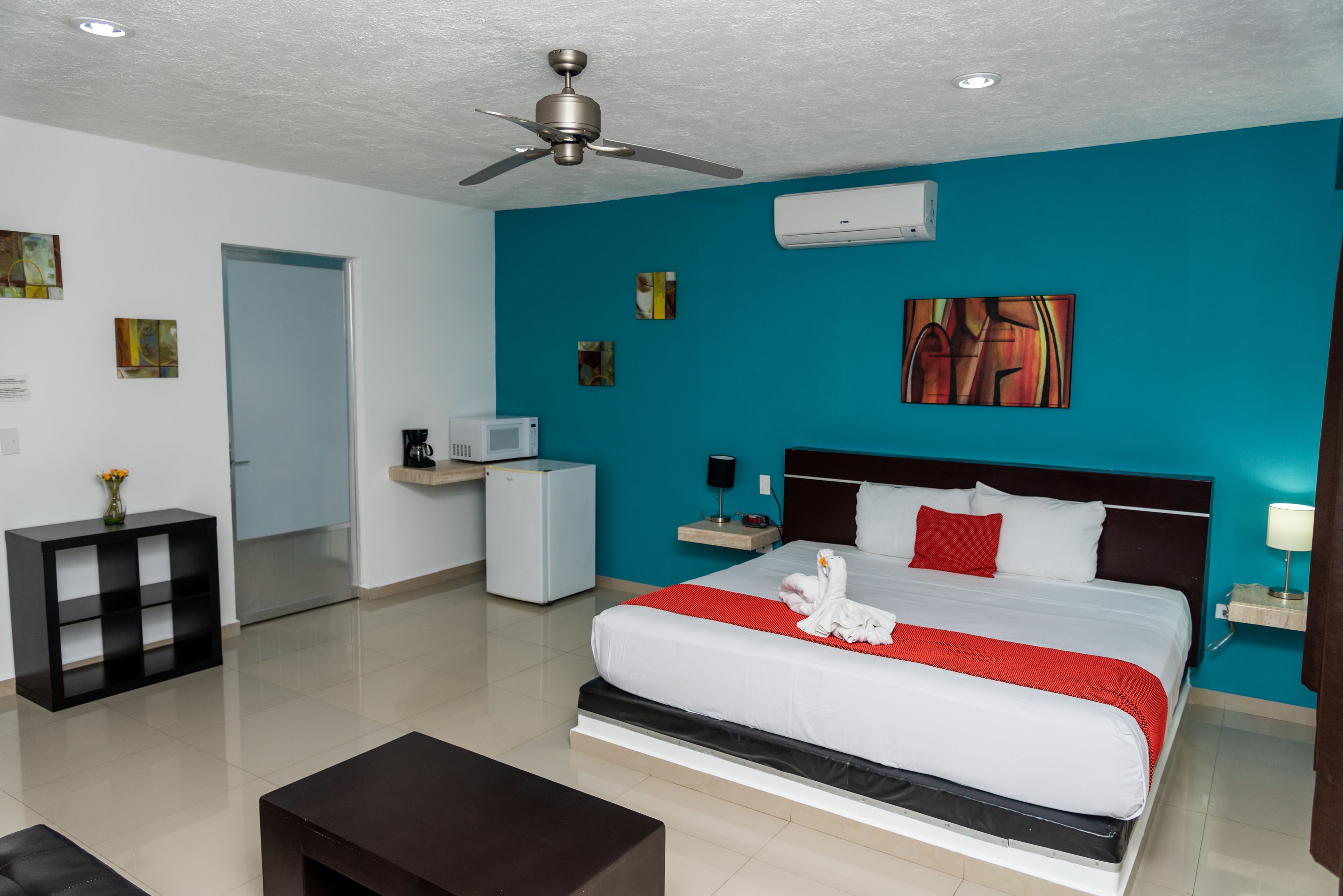 Una moderna camera d'hotel con un letto grande, una ventola a soffitto, una scrivania con un computer e opere d'arte alle pareti.