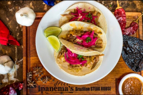 Un plato de tacos con carne deshebrada, repollo morado y gajos de lima, sobre una mesa de madera en un ambiente rústico.
