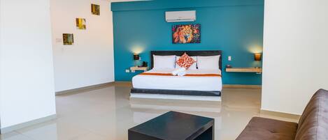 A modern hotel room with a large bed, a black coffee table, and a blue accent wall.