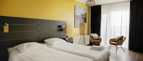 Ett hotellrum med två sängar, en sänggavel, en stol, en lampa och ett fönster med gardiner.