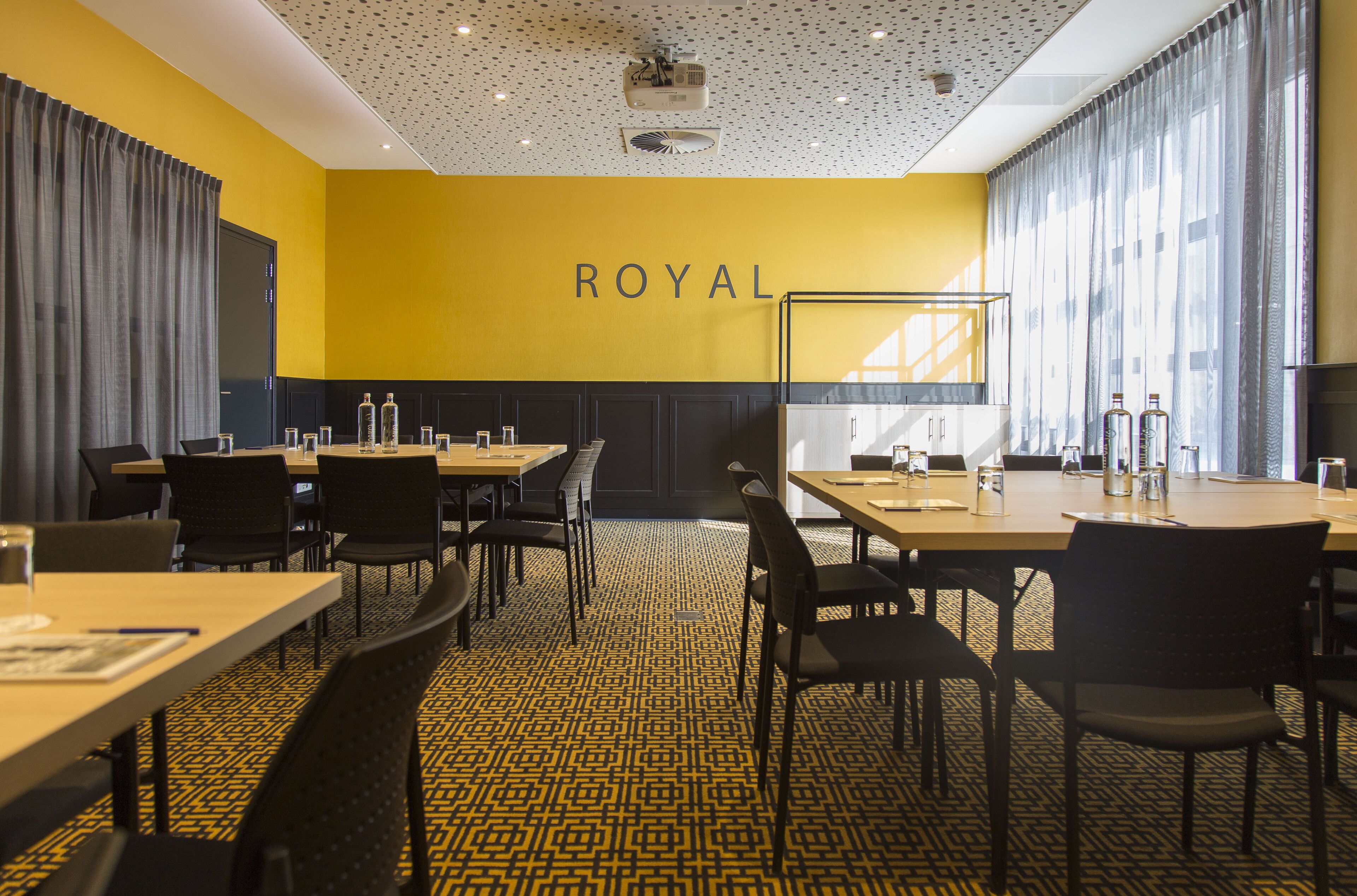 A conference room with a yellow wall, black chairs, and tables.