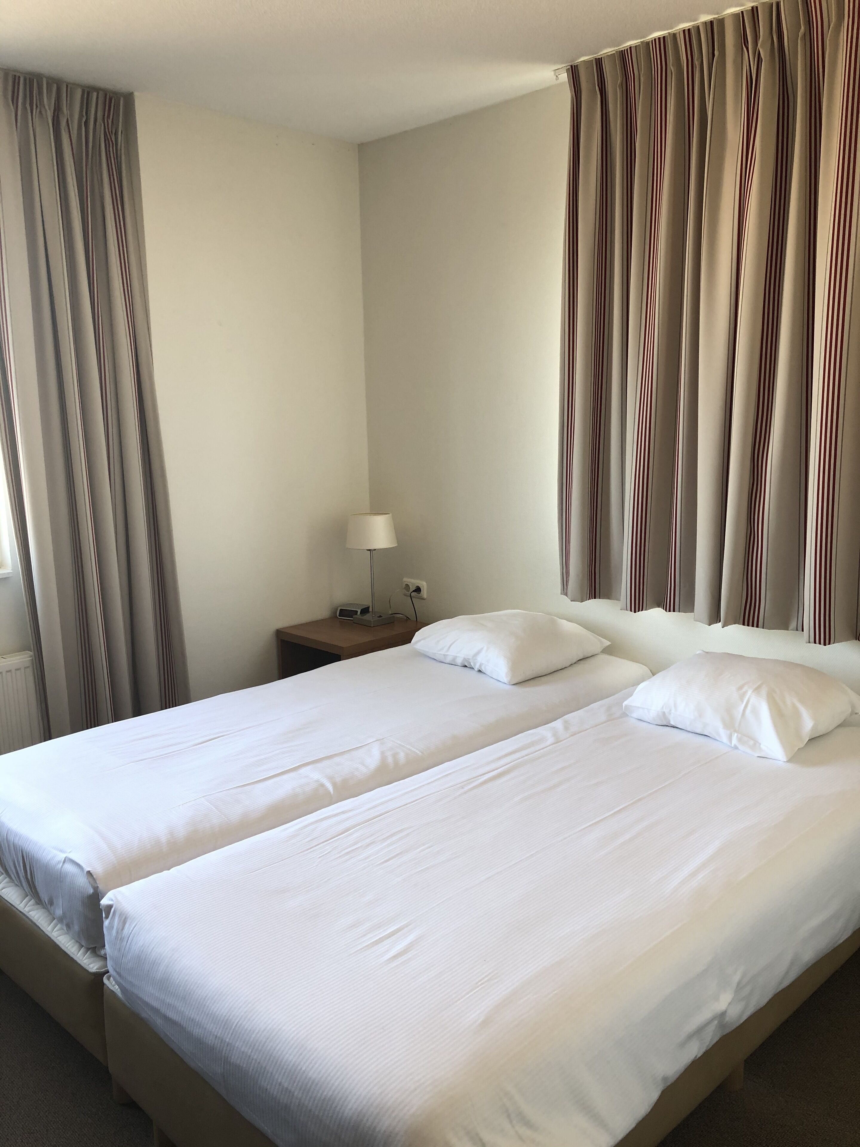 Une chambre d’hôtel avec deux lits, une table de chevet avec une lampe et des rideaux.